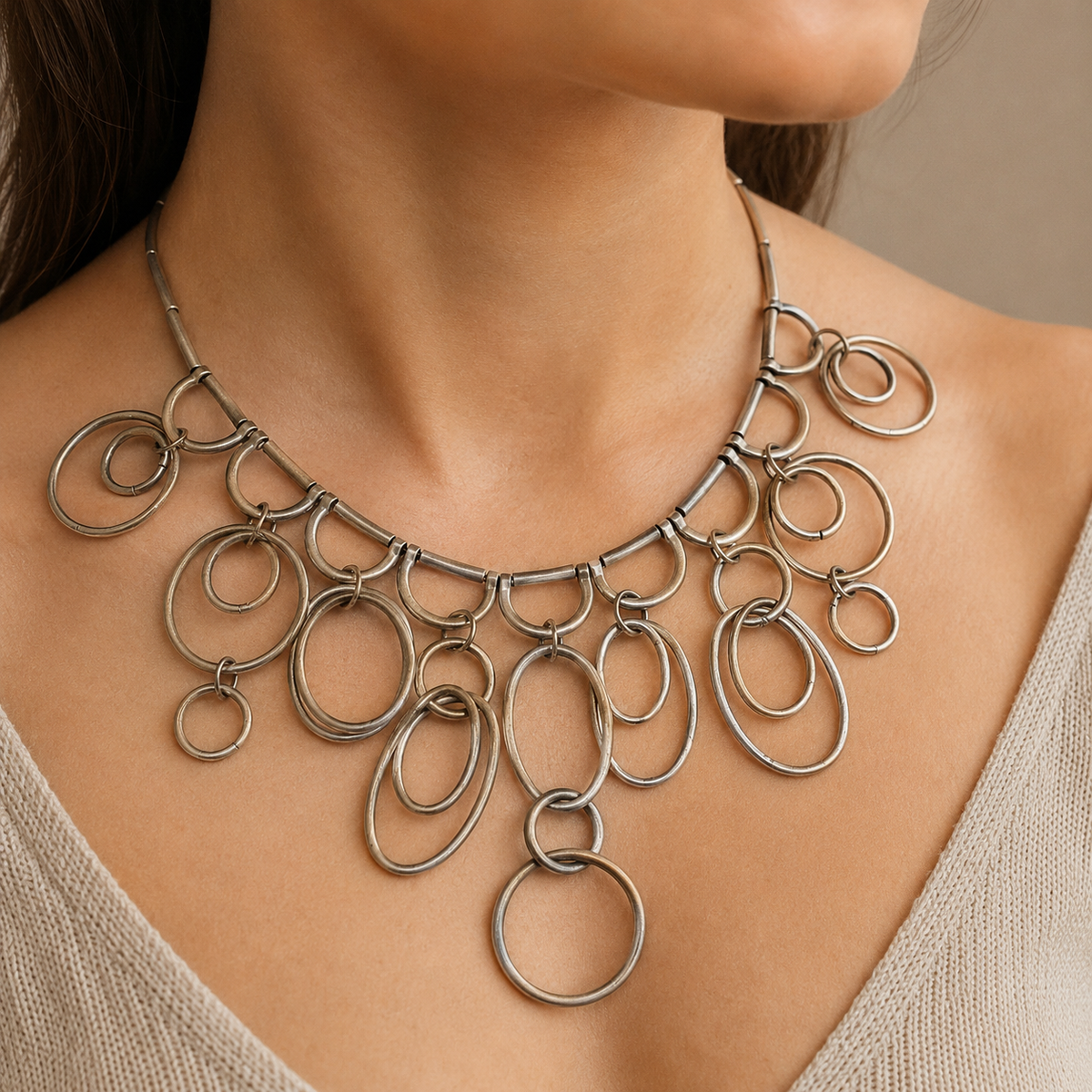 Silver-tone statement necklace with layered ring drops and a sculptural silhouette.