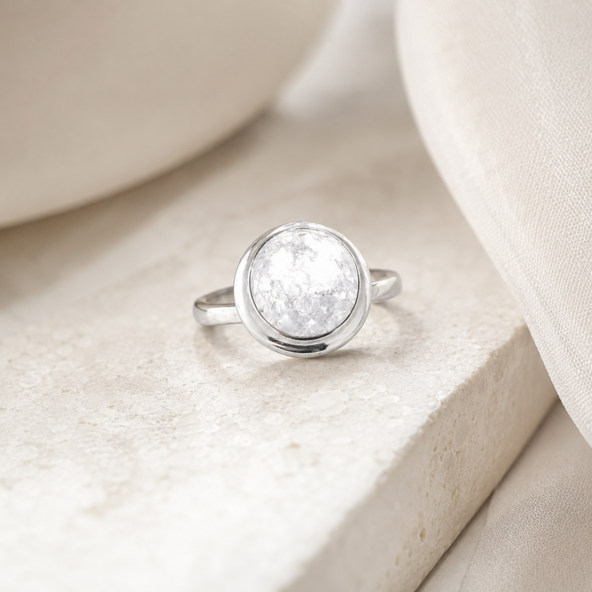 Minimalist silver-tone ring with a luminous clear center stone on a white background.
