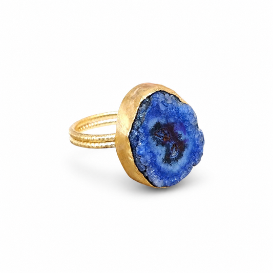 Blue druzy agate ring with a gold-tone setting on a white background.