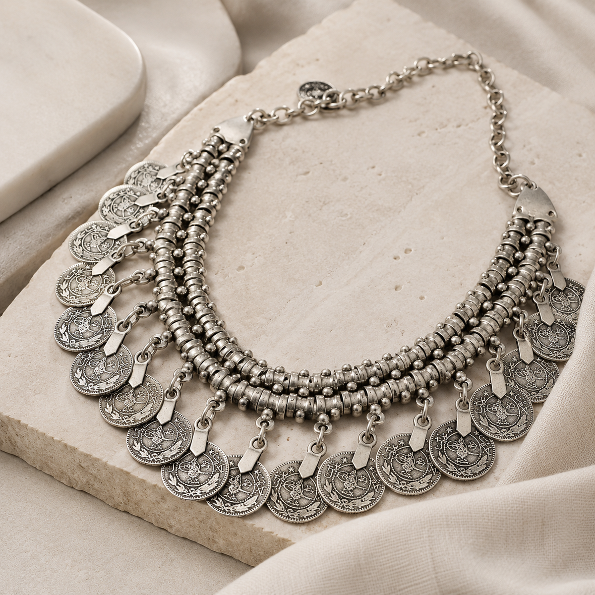 Angled view of a silver-tone coin fringe collar necklace with layered rows.