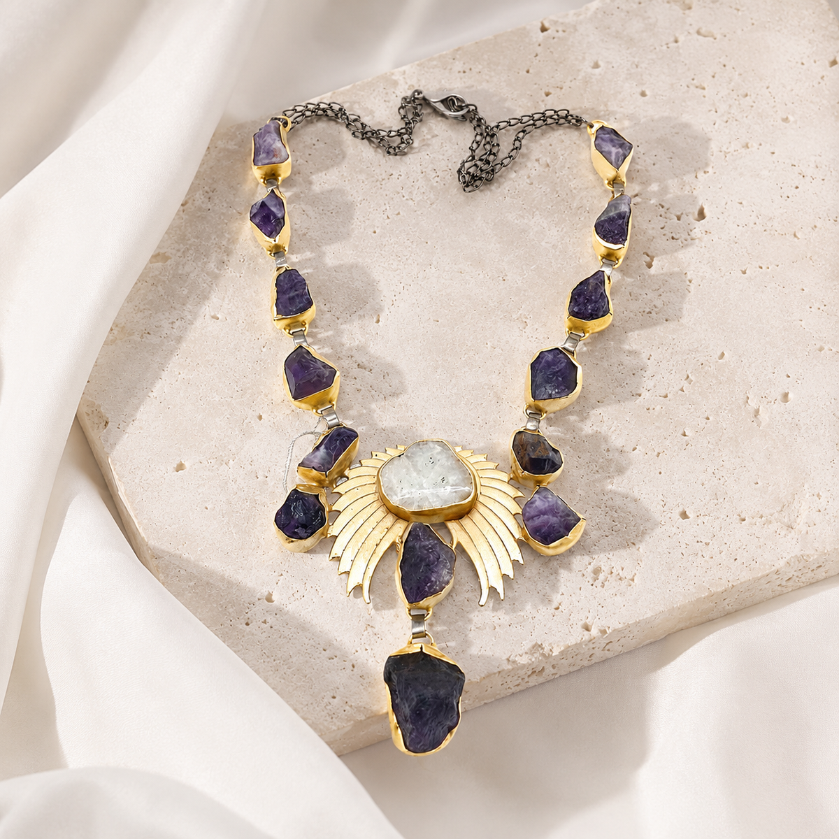 Gold-tone statement necklace with amethyst crystal-like stones arranged in a wing-inspired design.