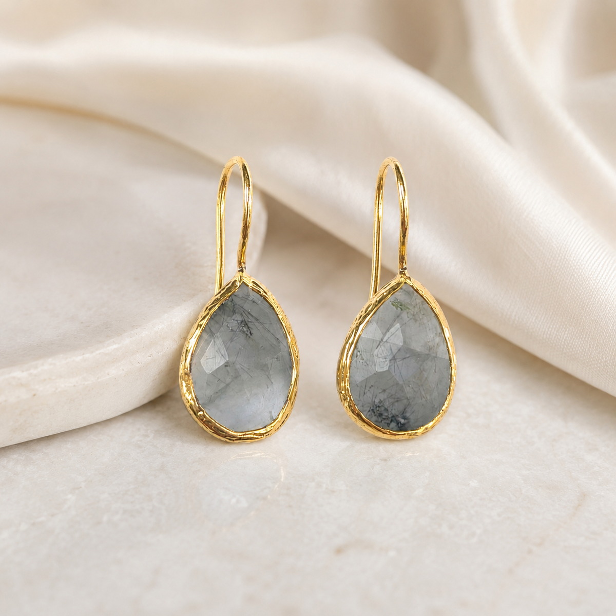 Pair of teardrop earrings with gray faceted stones and gold-plated frames on a white background.
