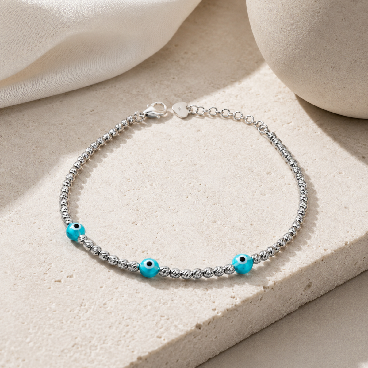 Silver bracelet with three blue evil eye accents in a clean product view.