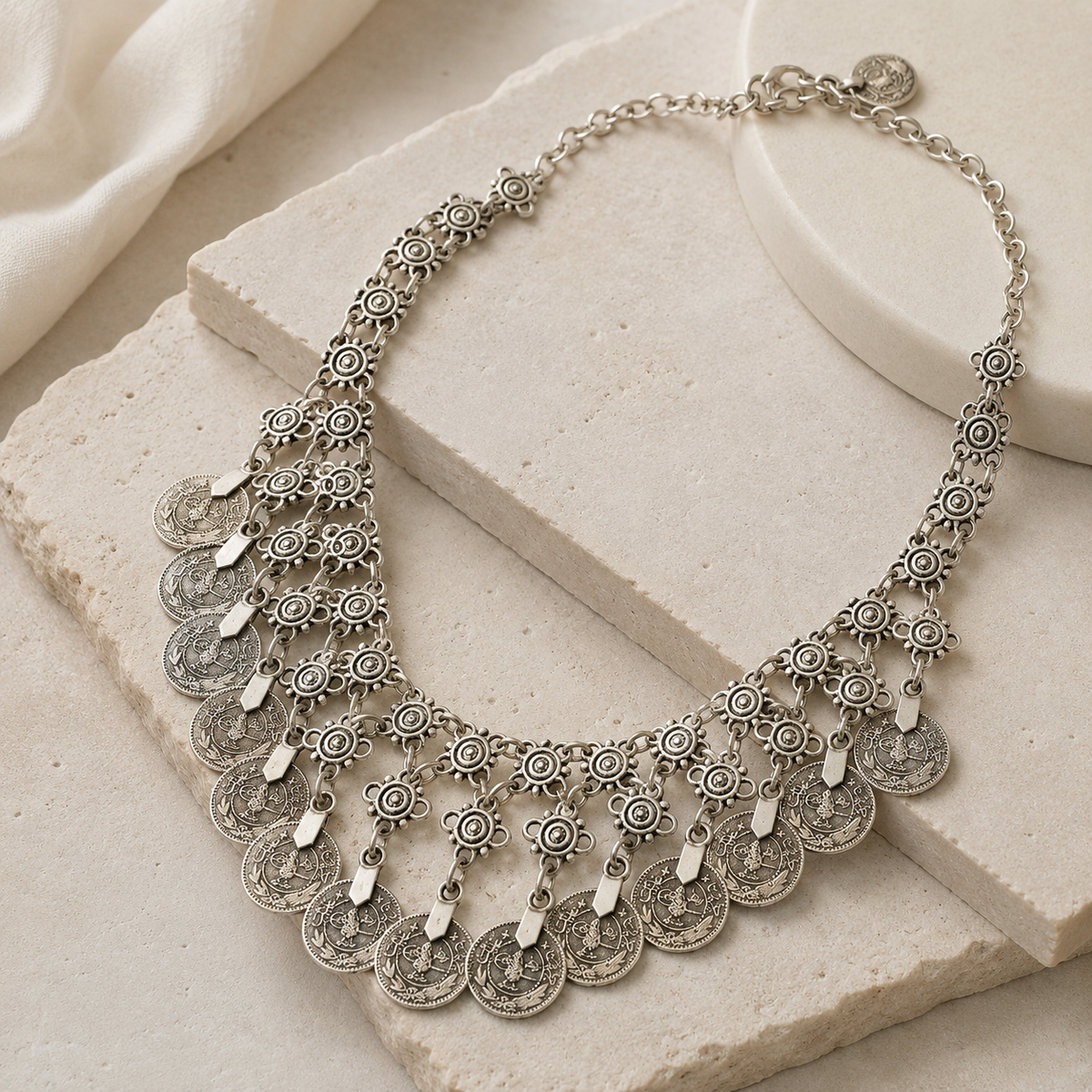 Angled view of a silver-tone statement necklace with coin fringe detail.