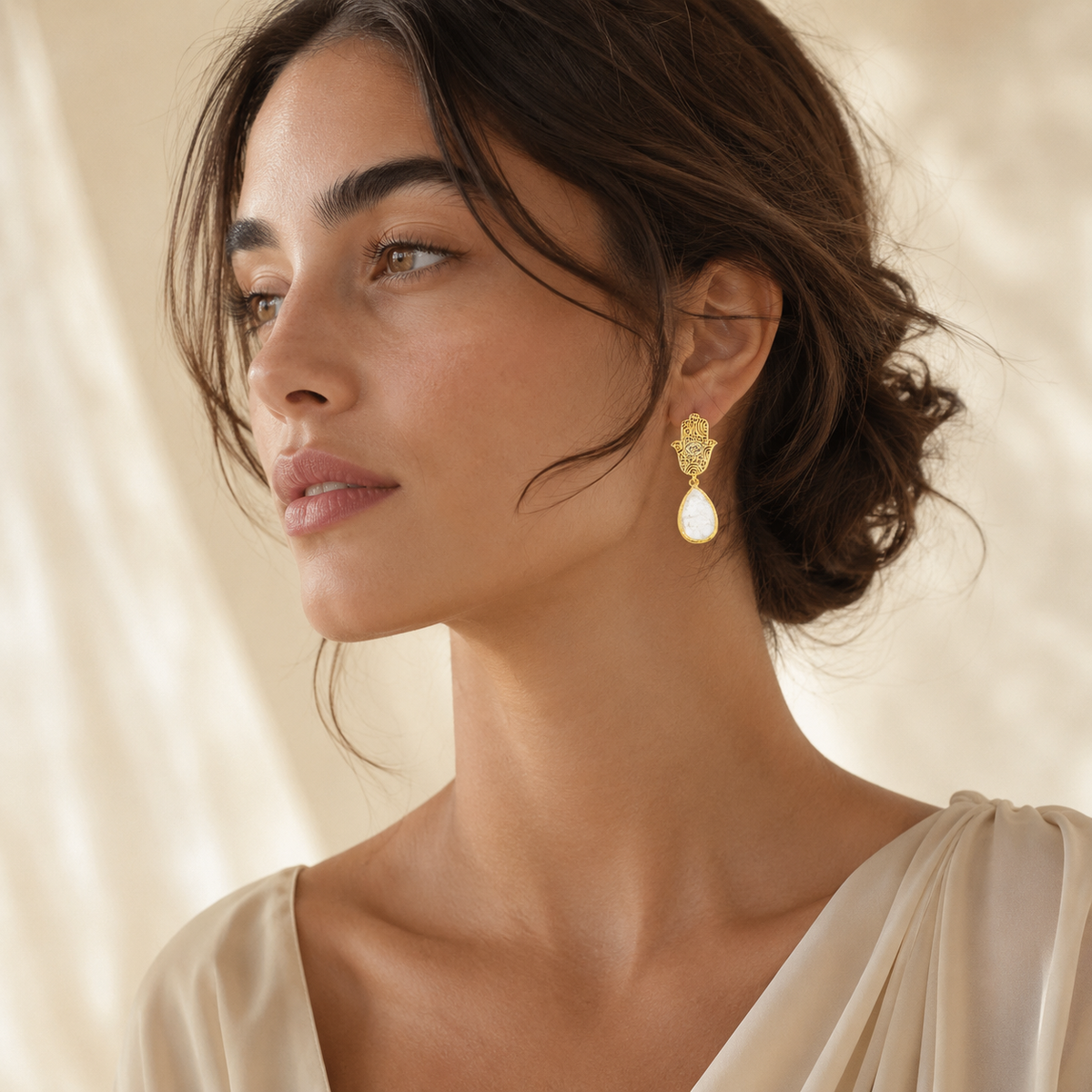 Decorative gold hamsa hand drop earrings with white teardrop stones.