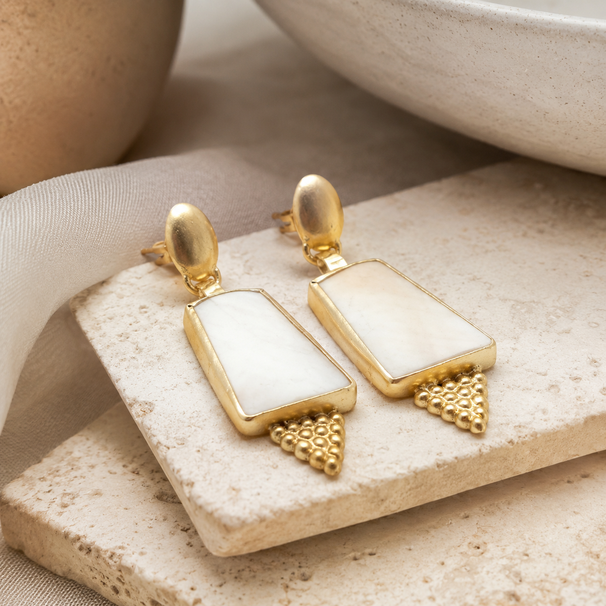 Angle view of gold-plated drop earrings with sculptural shield shapes and textured accents.