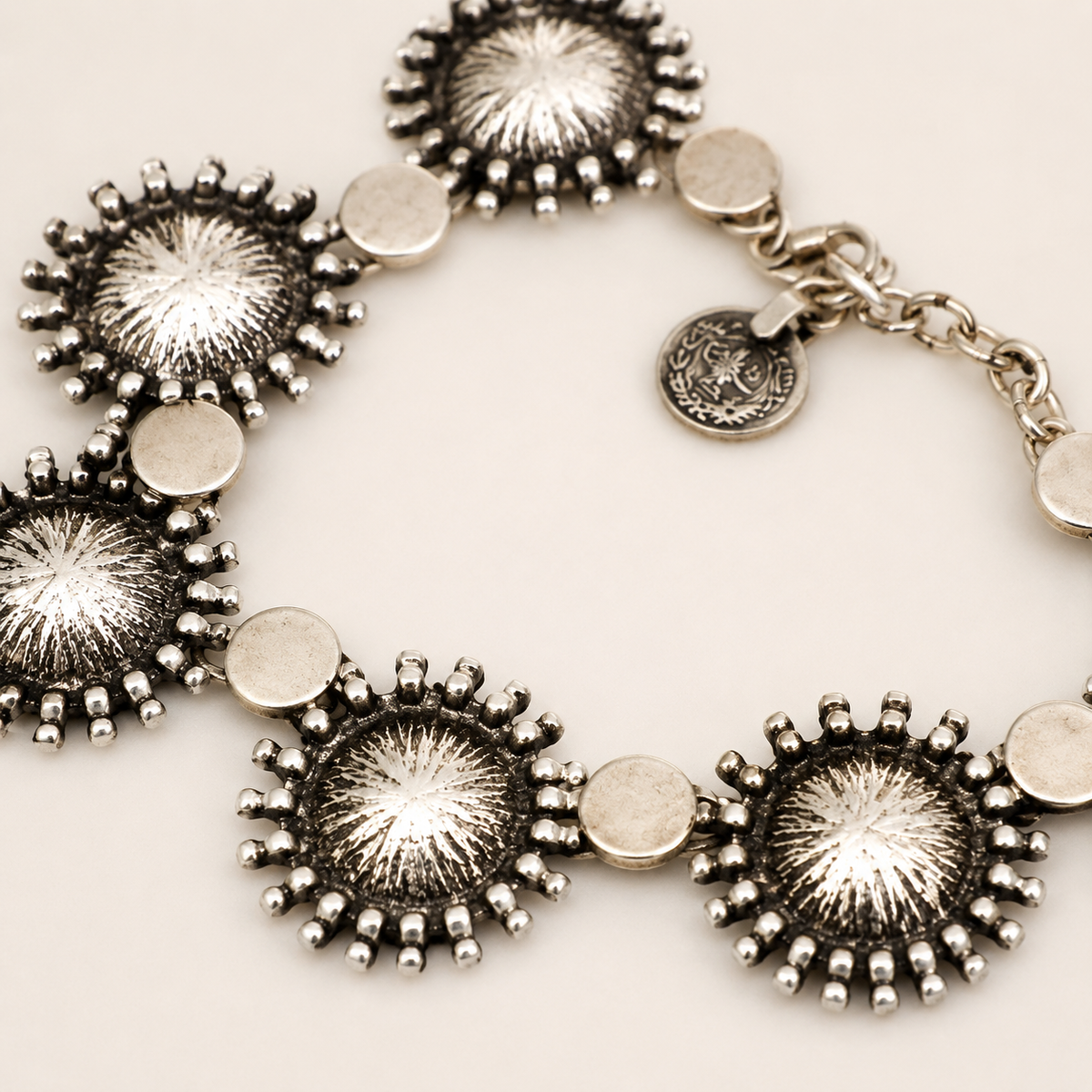 Close view of the silver-tone sunburst disc necklace with textured round links.