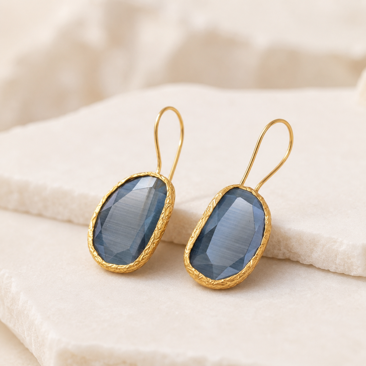 Angled view of gray teardrop earrings with a gold-plated setting.