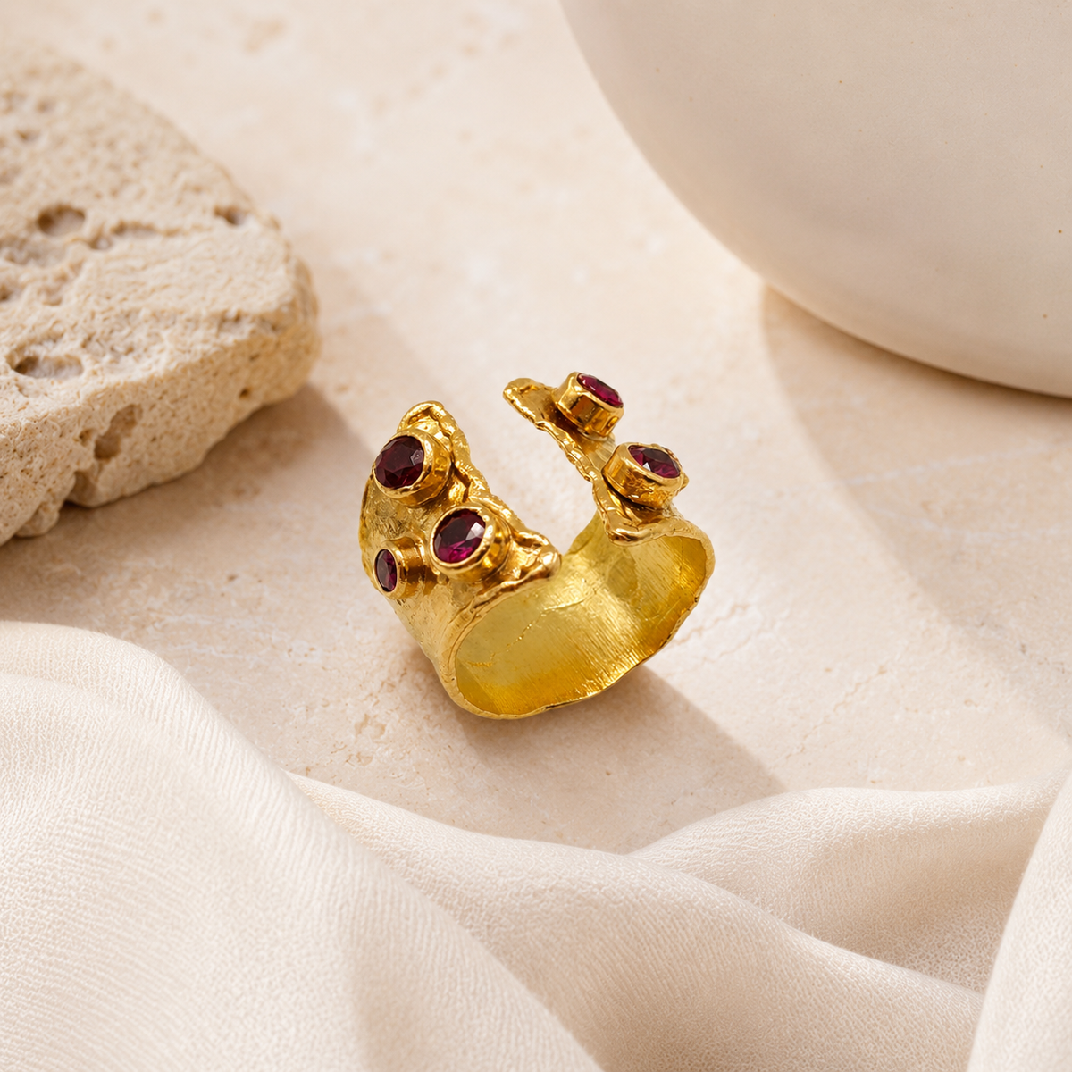 Gold open cuff ring with ruby pink stones and a bold sculptural silhouette.