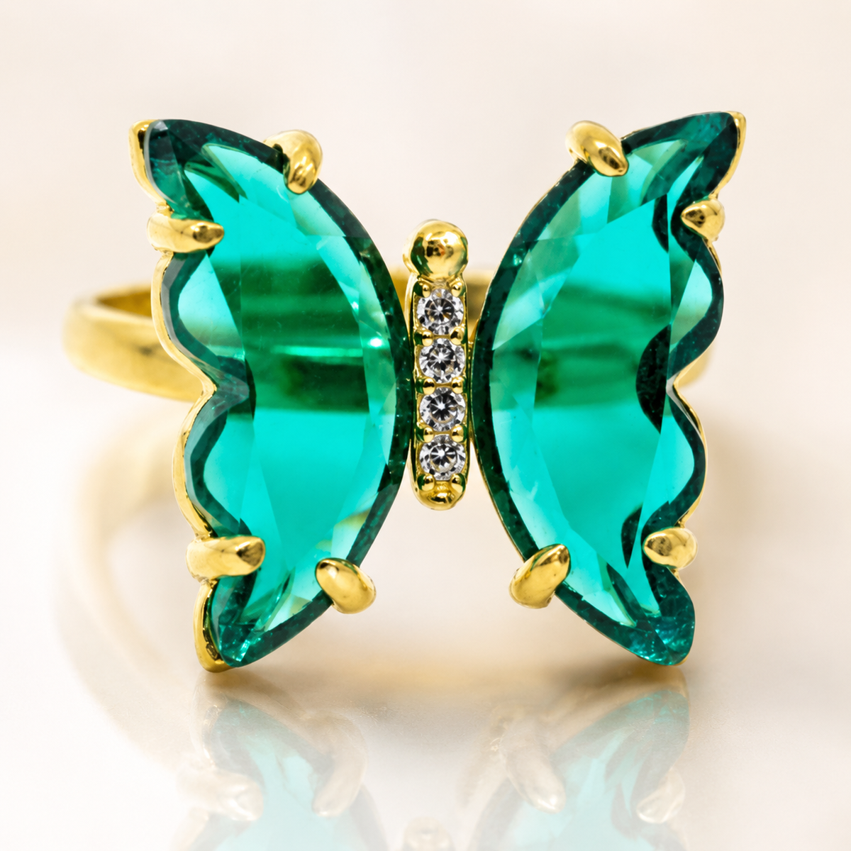 Close view of a gold-tone butterfly ring with faceted green stones.