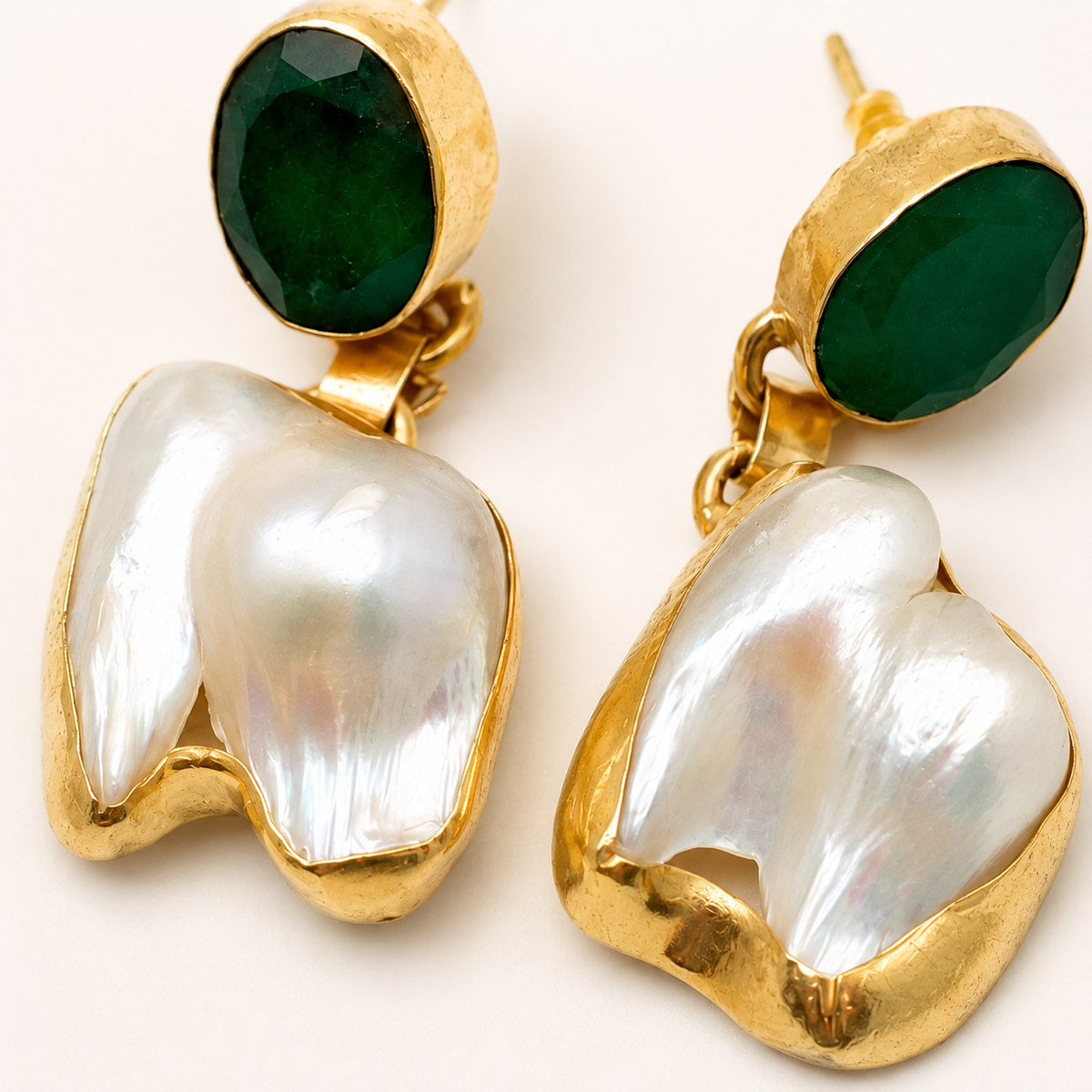 Close view of green stone and baroque pearl earrings in a gold-tone setting.