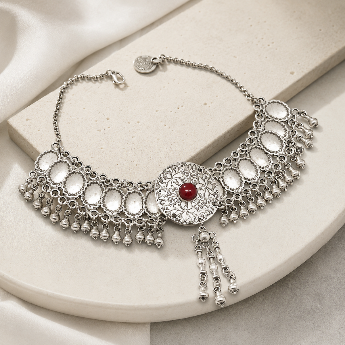 Angled view of a silver-tone statement necklace with textured discs and fringe drops.