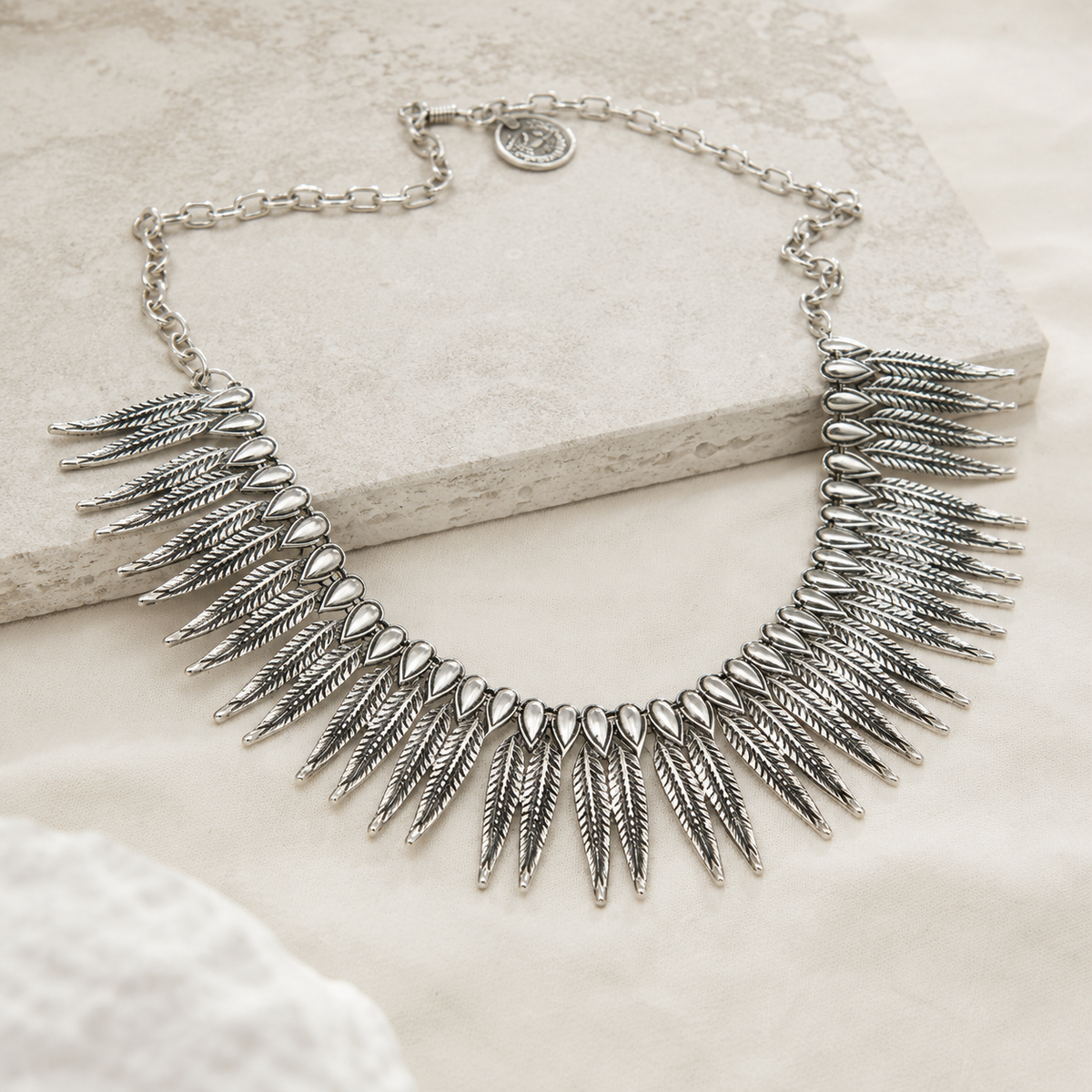 Angled view of a silver-tone collar necklace with textured leaf details.