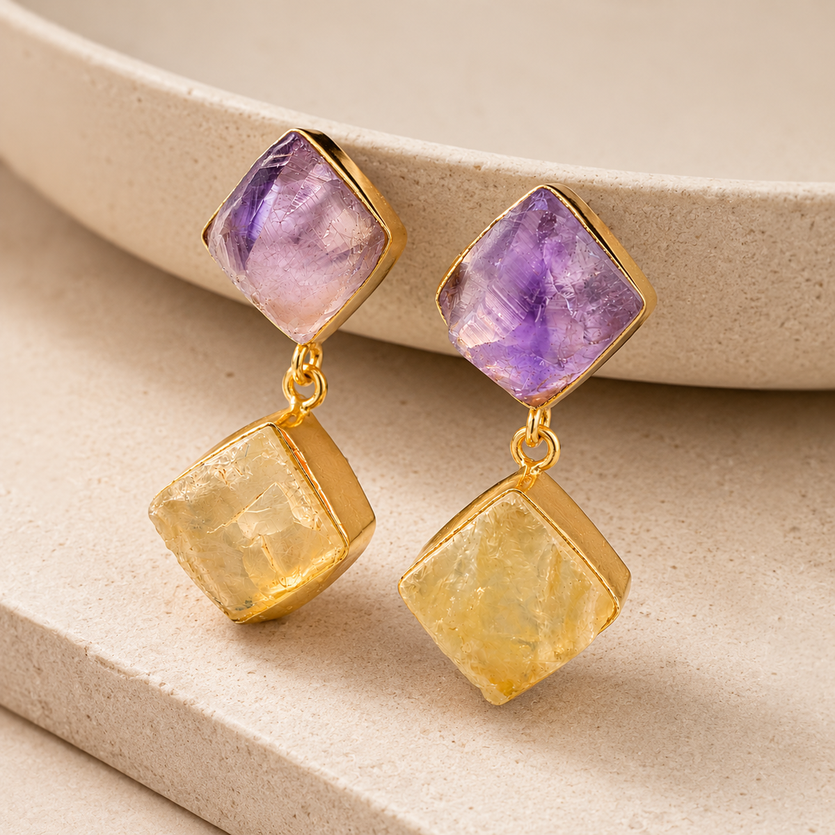 Angle view of gold-plated drop earrings with rough purple and golden stones.