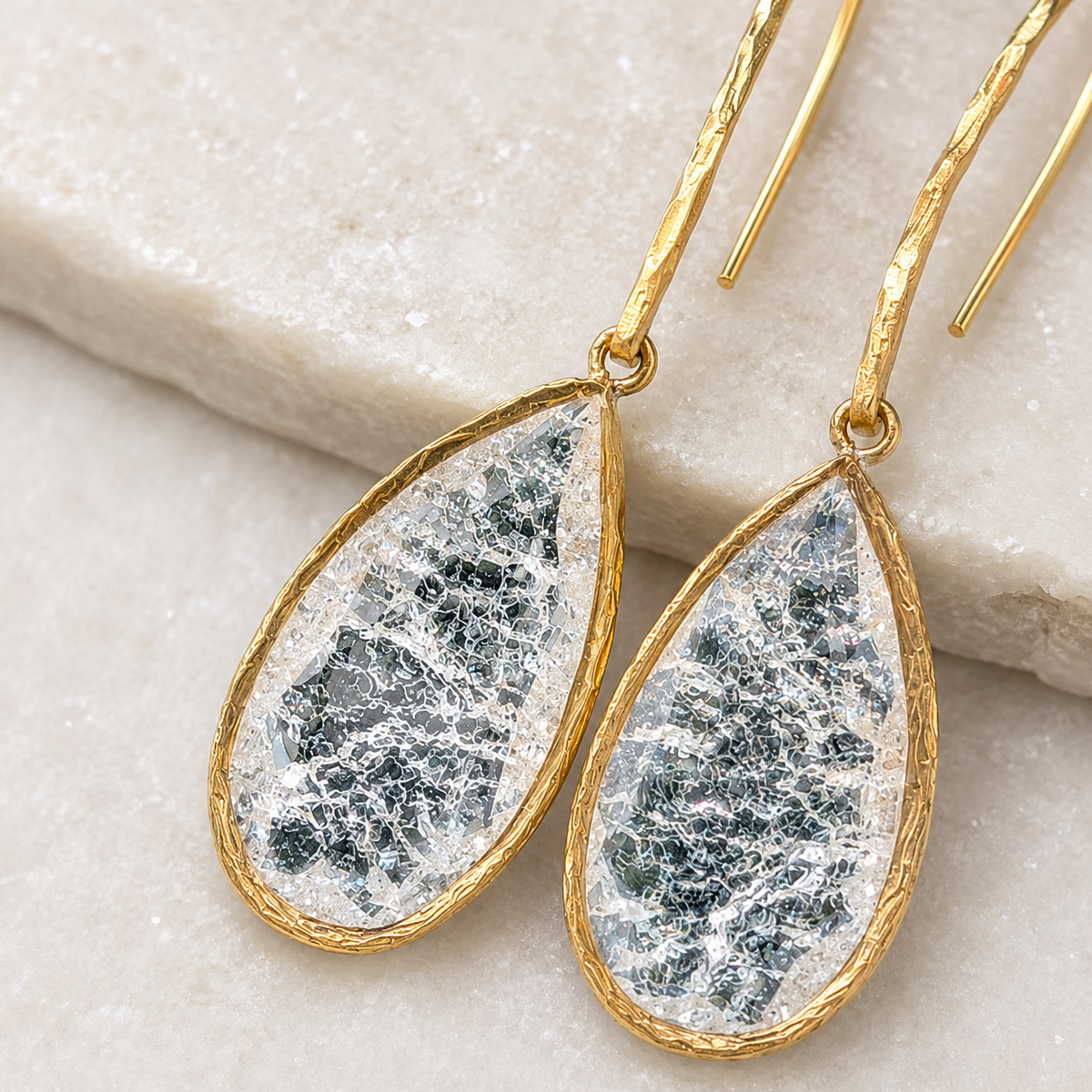 Close view of cracked crystal teardrop earrings with a gold-plated frame.