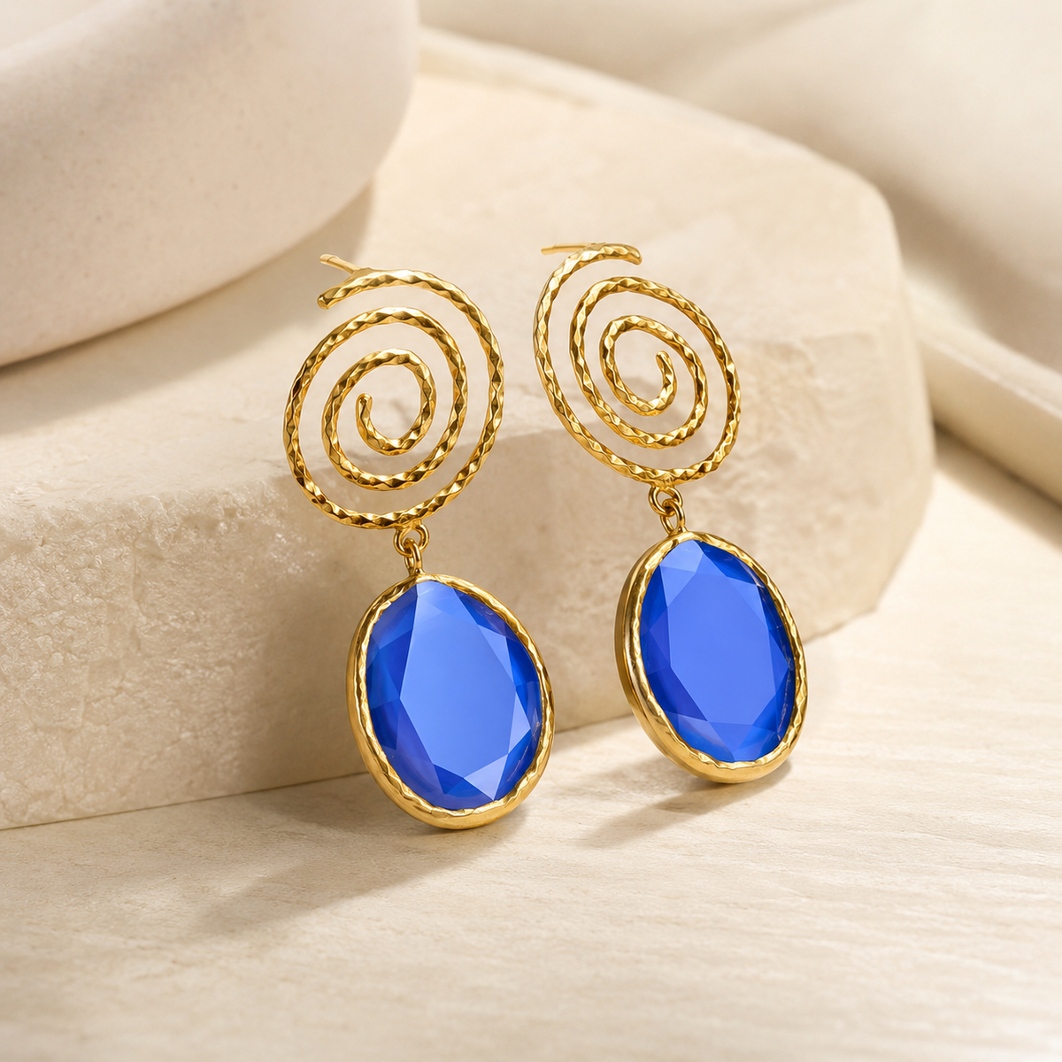 Angled view of gold-tone spiral drop earrings with navy blue stones.