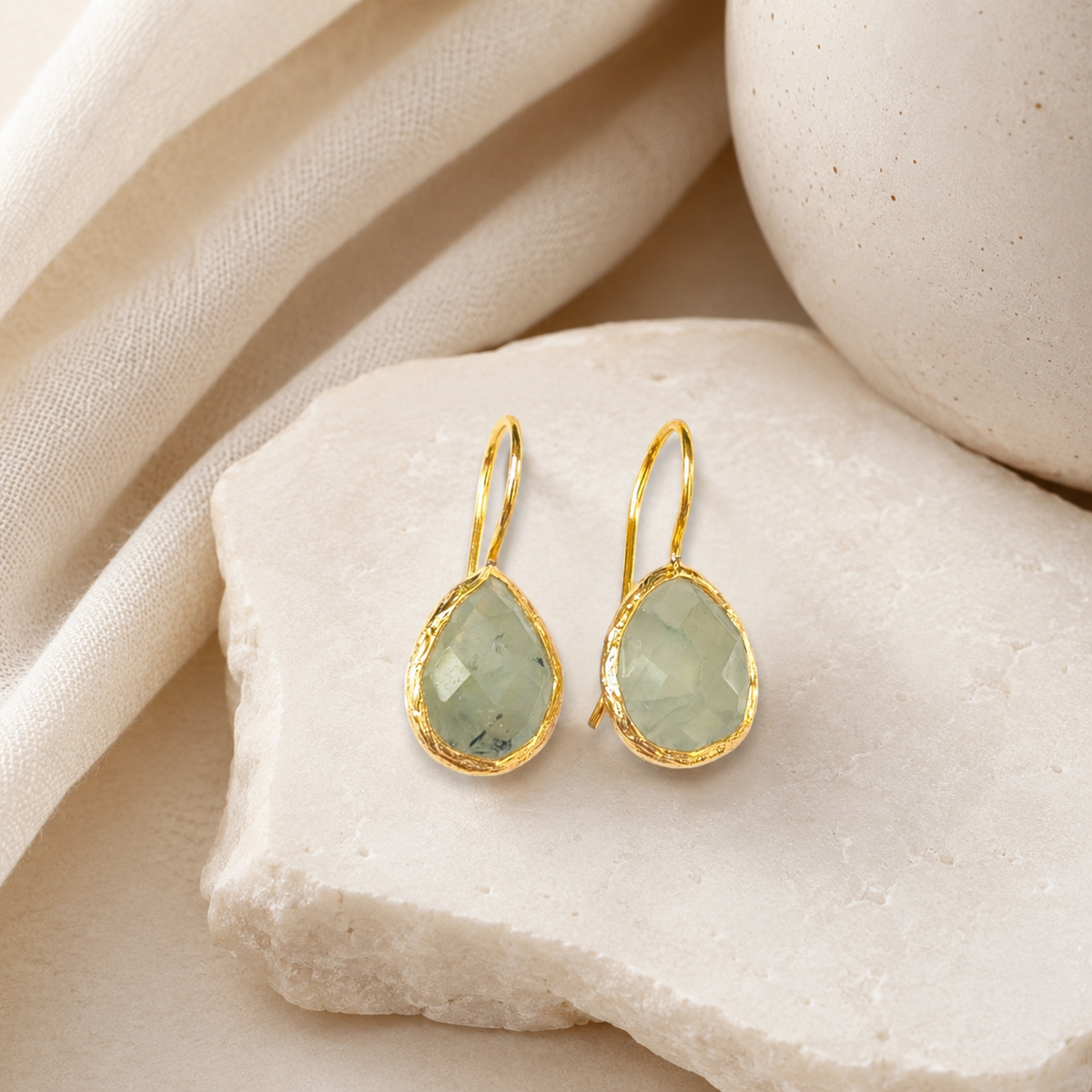 Gold drop earrings with green teardrop stones on a white background.