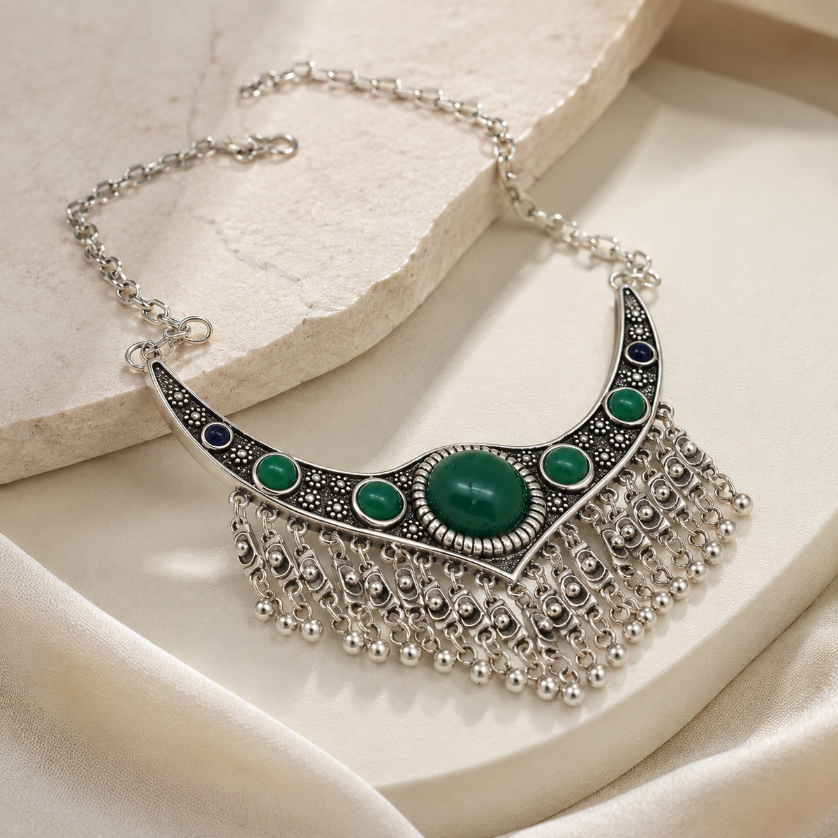 Angled view of a silver-tone fringe necklace with green stone accents.